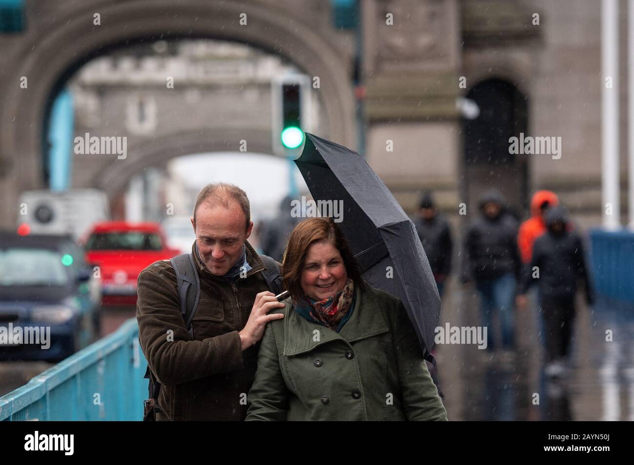 Die Menschen überqueren Tower Bridge in London während eines schweren Regenfluges, als Storm Dennis das Vereinigte Königreich trifft. Stockfoto