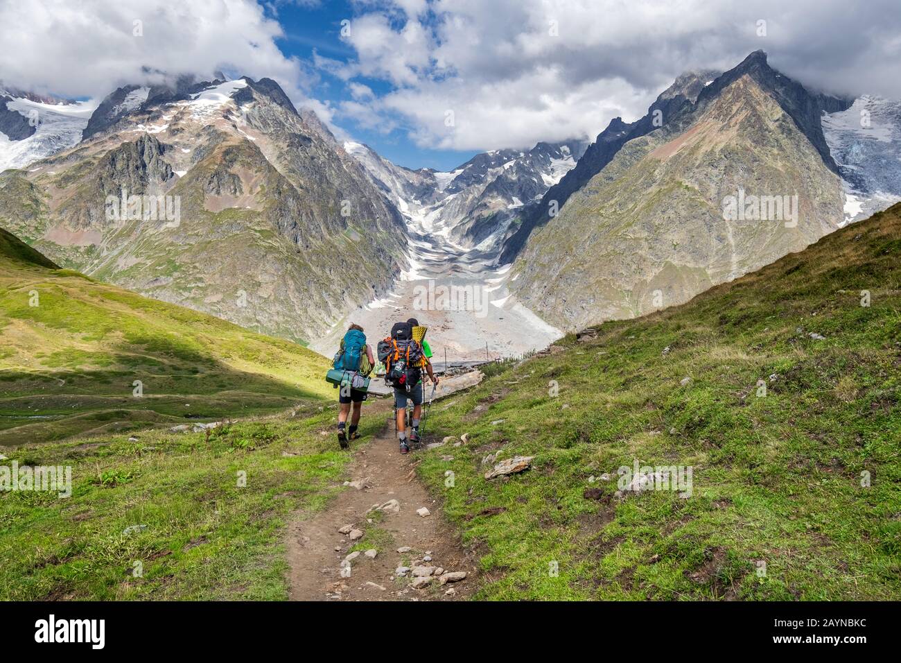Zwei Wanderer mit voller Campingausrüstung auf der Tour Do Mont-Blanc-Wanderung in den italienischen Alpen mit einem Gletscher und Bergen im Hintergrund Stockfoto Zwei Wanderer mit voller Campingausrüstung auf der Tour Do Mont-Blanc-Wanderung in den italienischen Alpen mit einem Gletscher und Bergen im Hintergrund Stockfoto