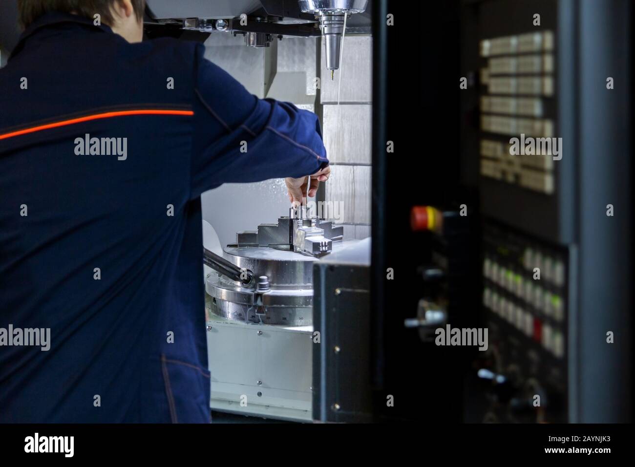 Der Bediener der 5-Achs-cnc-Fräsmaschine wechselt das Werkstück in einer Spannzange. Selektiver Fokus auf den Hintergrund. Stockfoto