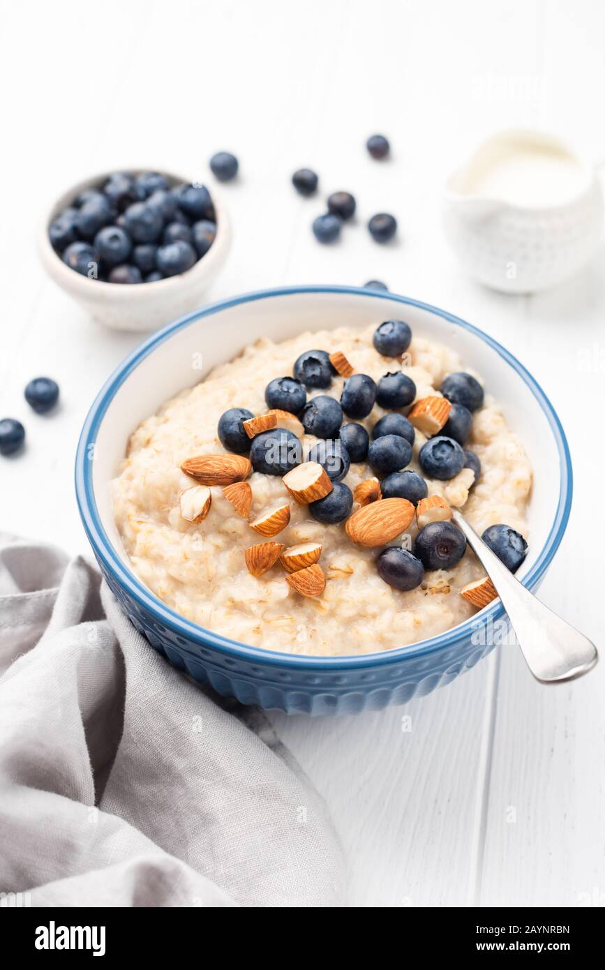 Schale mit Haferbrei mit Blaubeeren, Mandeln auf weißem Holztisch. Gesundes Frühstück, sauberes Esskonzept Stockfoto