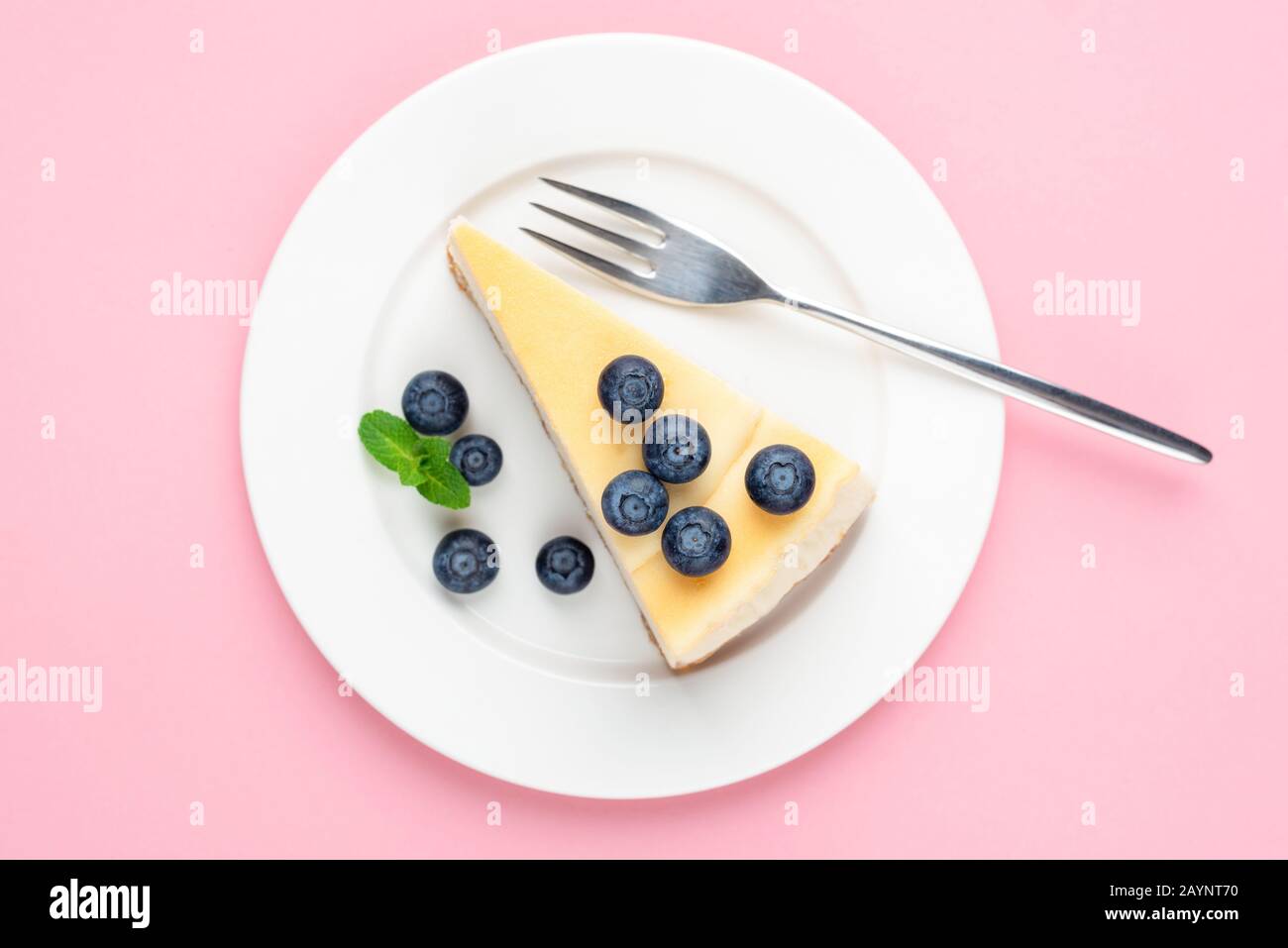 Käsekuchen mit Blaubeeren auf rosa Hintergrund. Draufsicht. Dessert des Mädchens. Klassischer einfacher New Yorker Käsekuchen auf weißem Teller Stockfoto