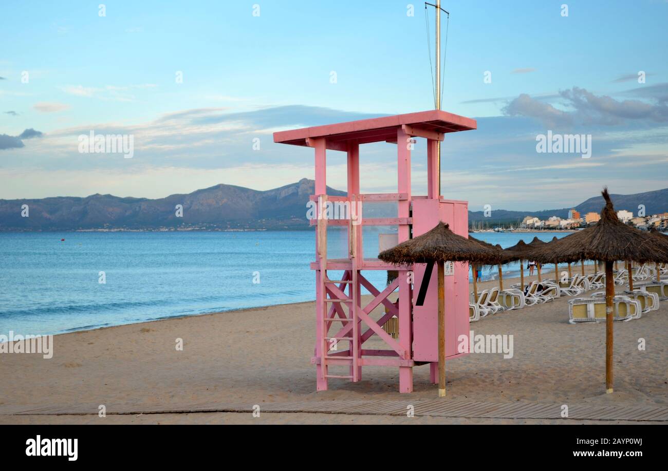 Reihe von Hängematten am Strand von Muro. Rosafarbener Rettungsdienst am Strand. Sonnenliegen und Sonnenschirme. Stockfoto