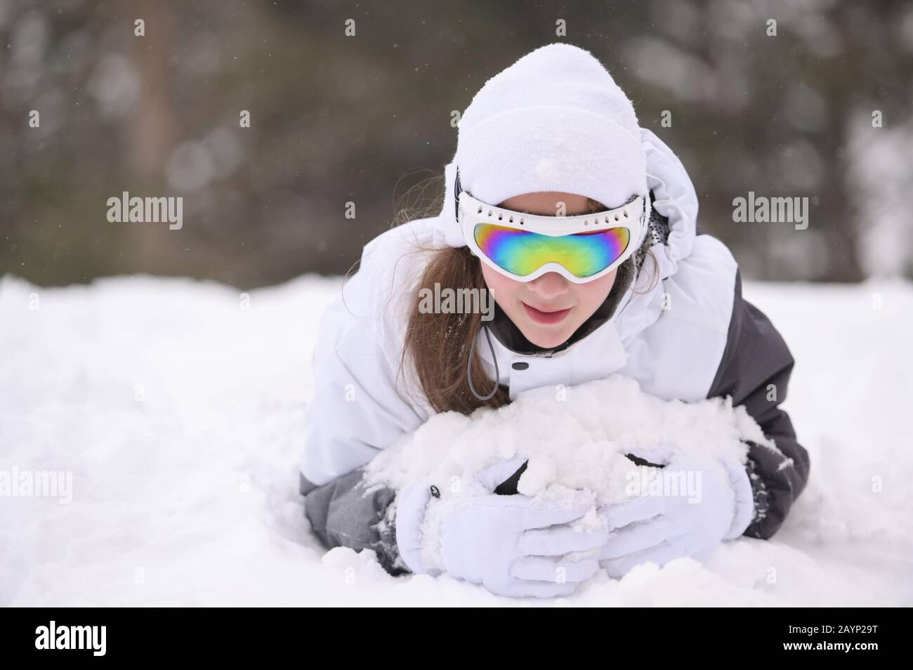 Fröhlich lächelnd schönes kleines Mädchen in Wollmütze und Skibrille, die im Winter in weißem Schnee während der Bergwaldfreizeit liegt Stockfoto