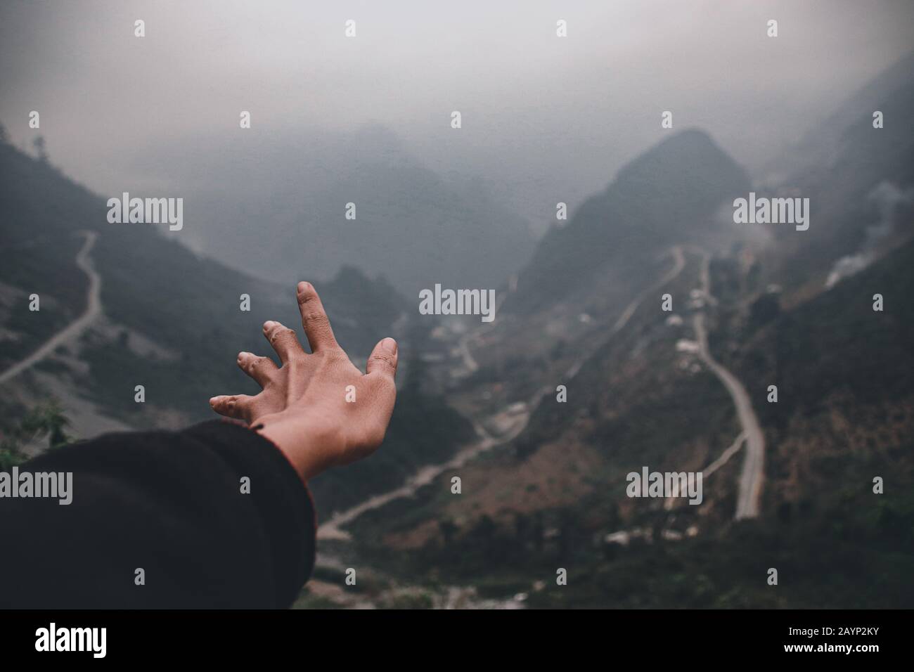 Eine Hand, die zu den nebligen Bergen und kurvenreichen Straßen von ha giang Loop in Vietnam reicht und ein filmisches und stimmungsvolles Reisefoto zeigt Stockfoto