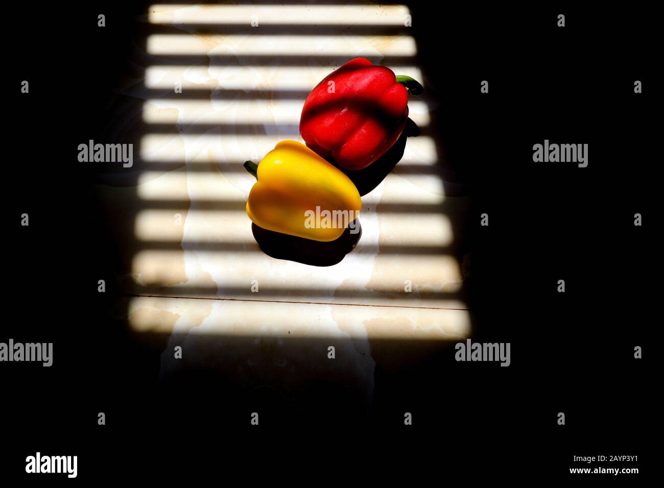 Gelbe und rote Paprika mit gestreiften Schattenlinien aus einem Fenster, um das Konzept von Gastronomie, Ernährung und Veganismus zu zeigen Stockfoto