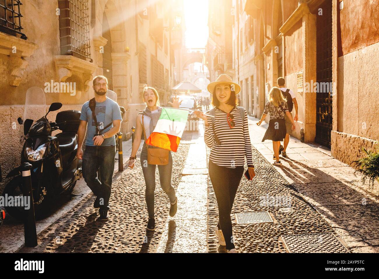 Drei junge Freunde Touristen, die mit italienischer Flagge die Stadtstraße hinuntergehen Stockfoto