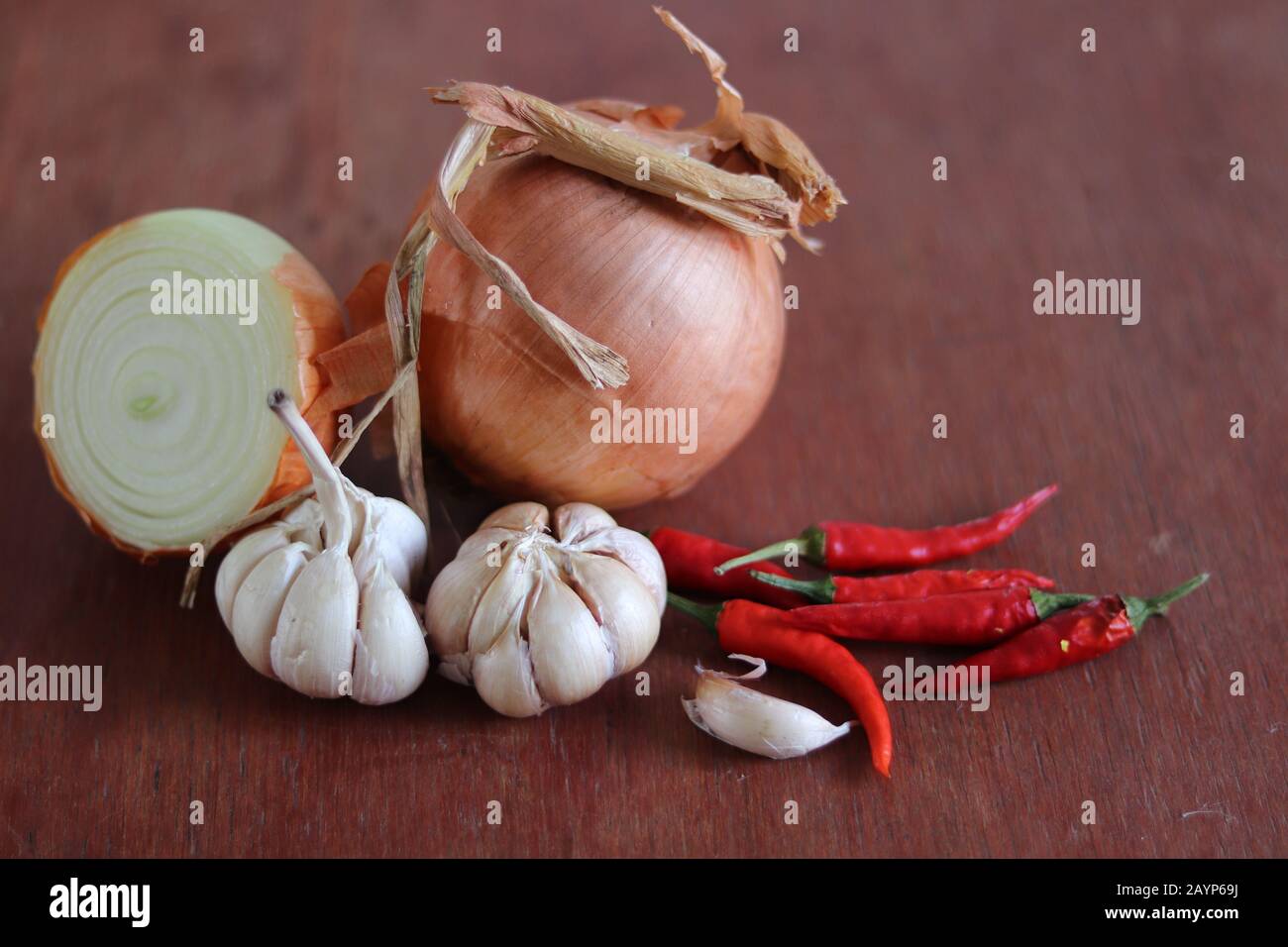 Zwiebel, Knoblauch und rote Chilis vor Holzhintergrund, um das Konzept der Gastronomie, Küche und Lebensmittelindustrie zu zeigen Stockfoto