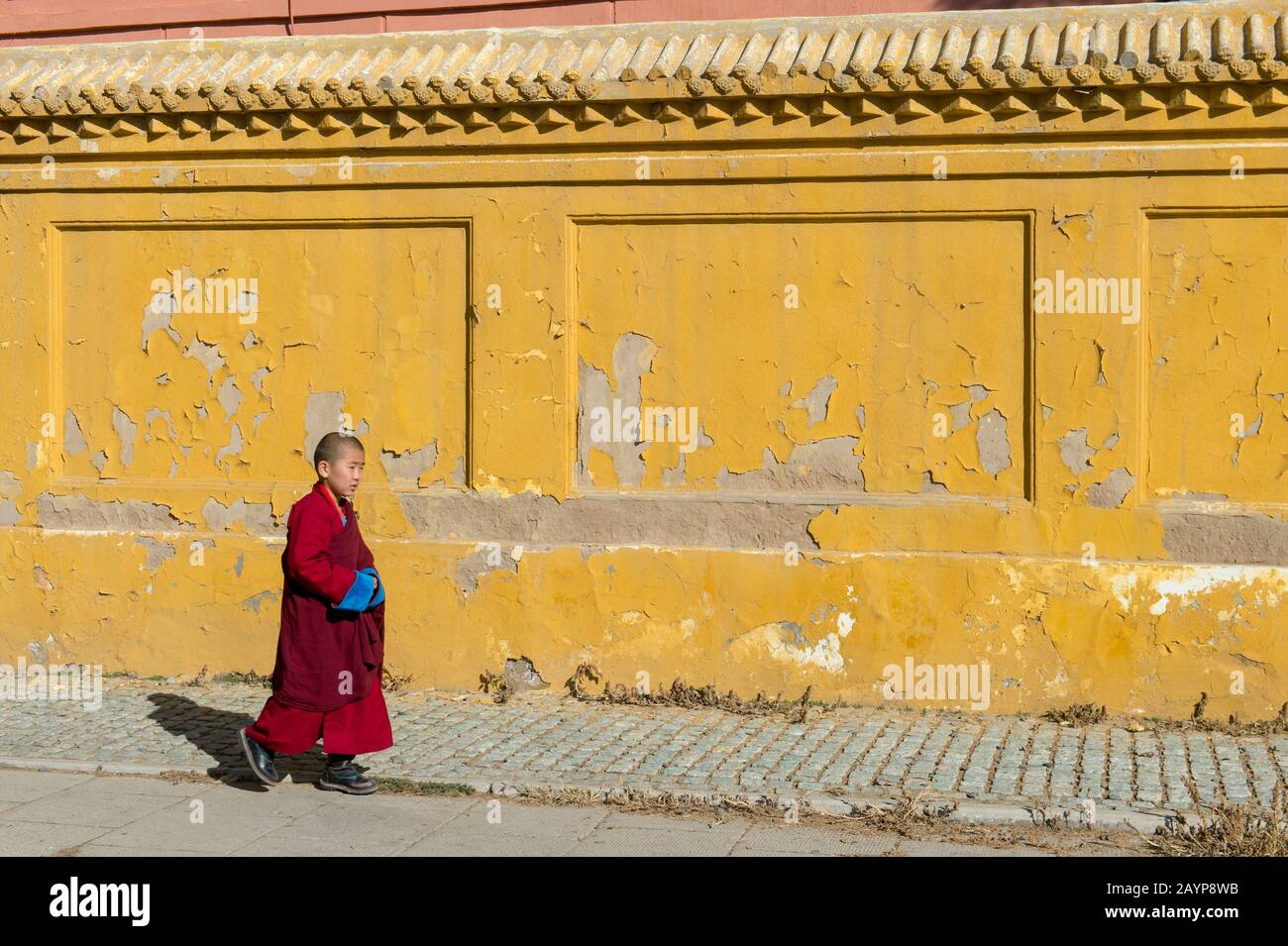 Ein junger Mönch spazieren vor einer gelben Wand des Klosters Gandantegchinlen in Ulaanbaatar, der Mongolei. Stockfoto