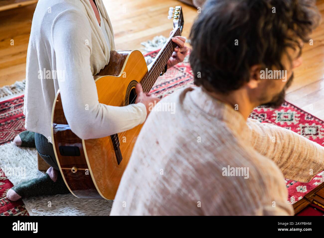 Junge schamanische Frau, die klassische Gitarre spielt, während sie neben dem Mann sitzt, der gemeinsam Harmonium als heilige Musik für die Meditation im Raum spielt Stockfoto