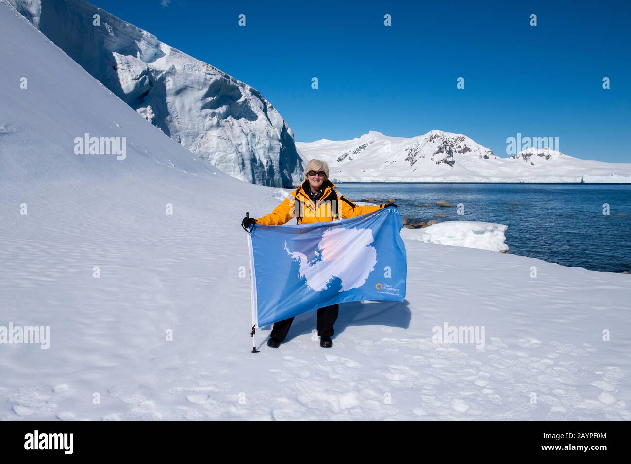 Antarktis, Antarktische Halbinsel, Nördliche Gerlache, Charlotte Bay. Expeditionfotograf und Abenteuerreisender Cindy Miller Hopkins mit Flagge. Stockfoto
