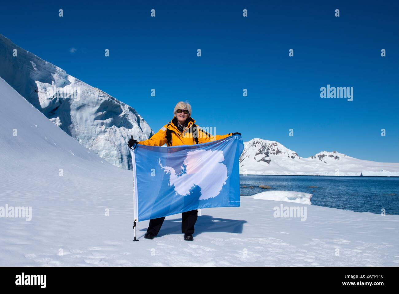 Antarktis, Antarktische Halbinsel, Nördliche Gerlache, Charlotte Bay. Expeditionfotograf und Abenteuerreisender Cindy Miller Hopkins mit Flagge. Stockfoto