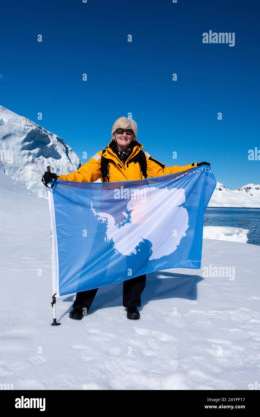 Antarktis, Antarktische Halbinsel, Nördliche Gerlache, Charlotte Bay. Expeditionfotograf und Abenteuerreisender Cindy Miller Hopkins mit Flagge. Stockfoto