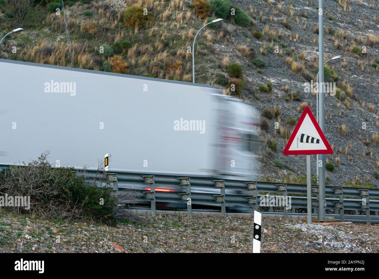 Verkehrswarnzeichen für die Gefahr starker Winde mit einem LKW, der die Autobahn passiert und sich bewegt. Stockfoto