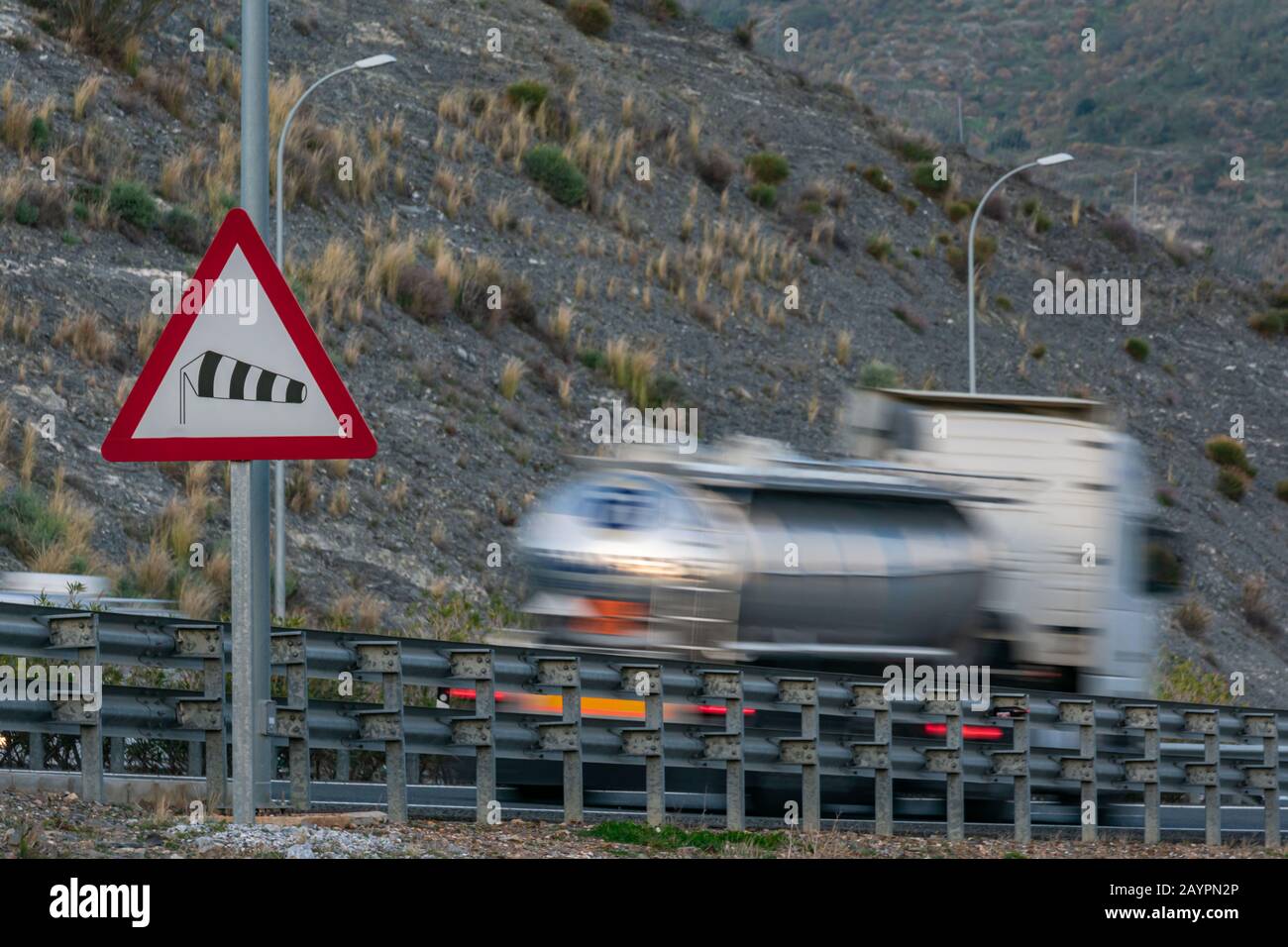 Verkehrswarnzeichen für die Gefahr starker Winde mit einem LKW, der die Autobahn passiert und sich bewegt. Stockfoto