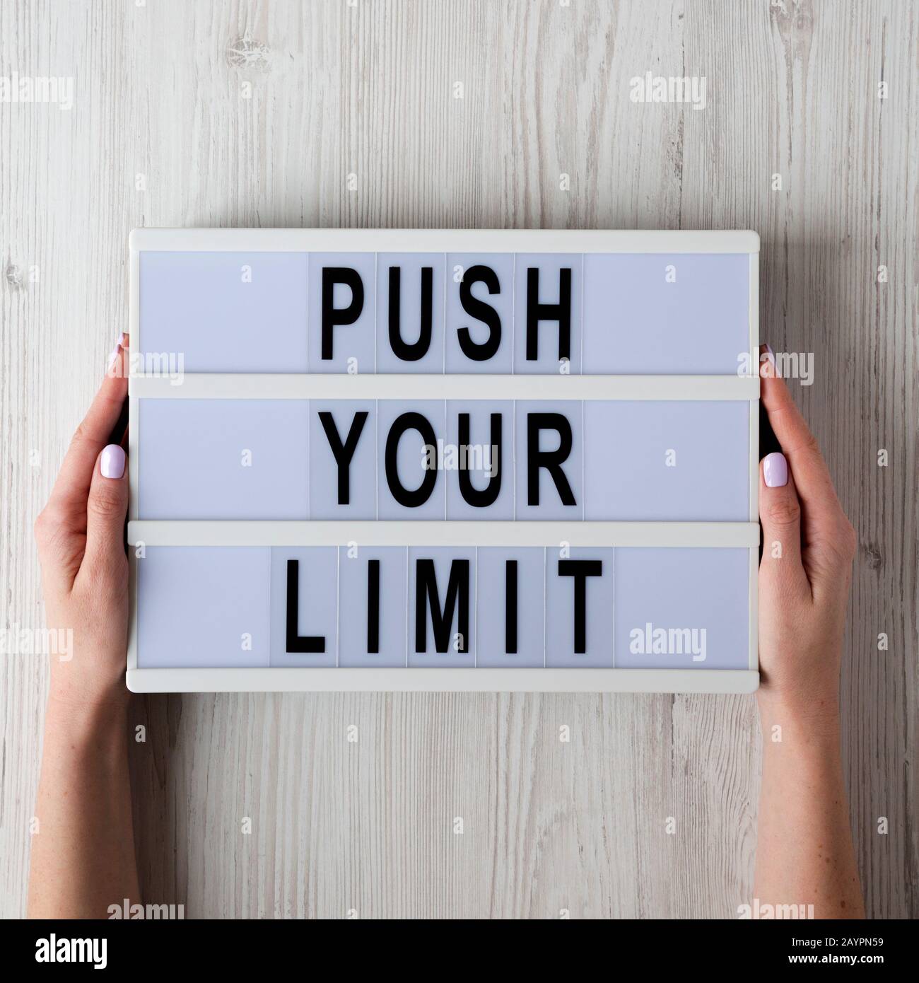 Weibliche Hände halten einen Leuchtkasten mit "Push Your Limit"-Worten über weiße Holzoberfläche, Draufsicht. Oben, von oben, flach. Stockfoto