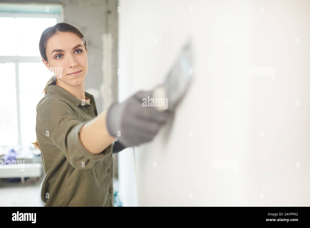 Porträt der lächelnden jungen Frau Glättung der Wand während der Renovierung Haus, Kopie Raum Stockfoto