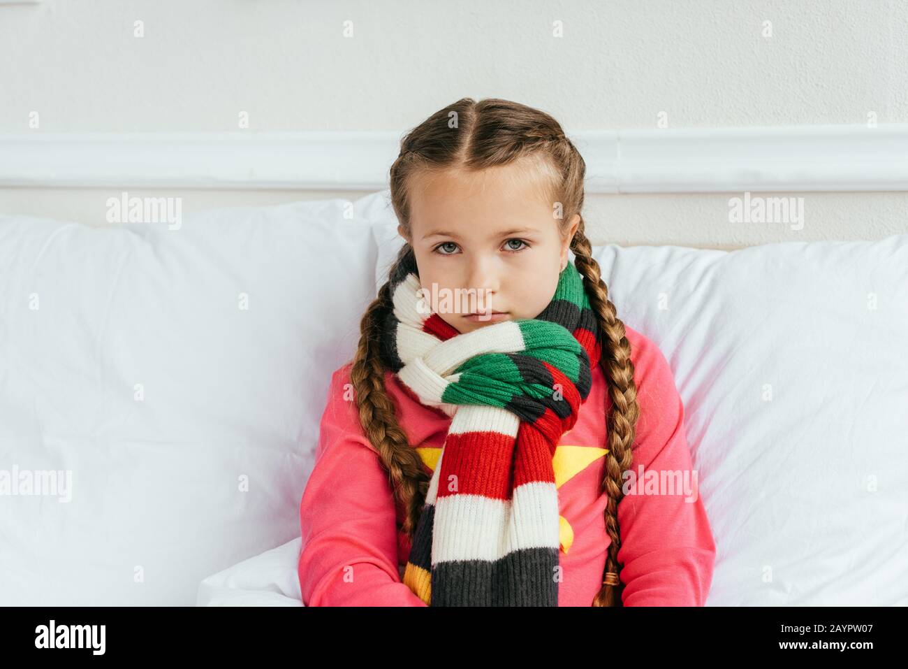 Trauriges krankes Kind im Schal, das auf dem Bett sitzt Stockfoto