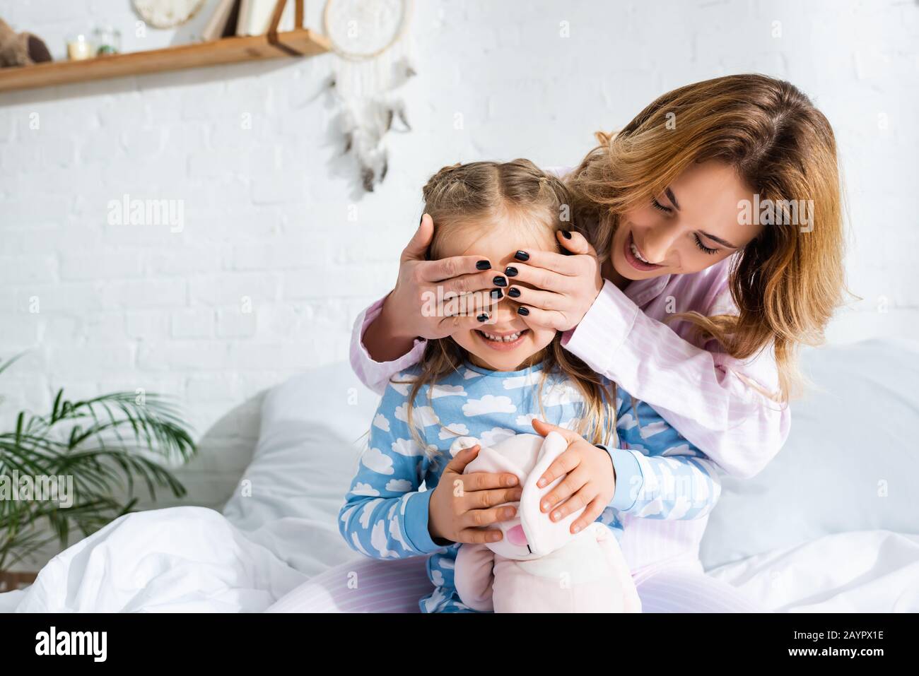 Lächelnde und attraktive Mutter verdunkelt im Schlafanzug das Gesicht der Tochter Stockfoto