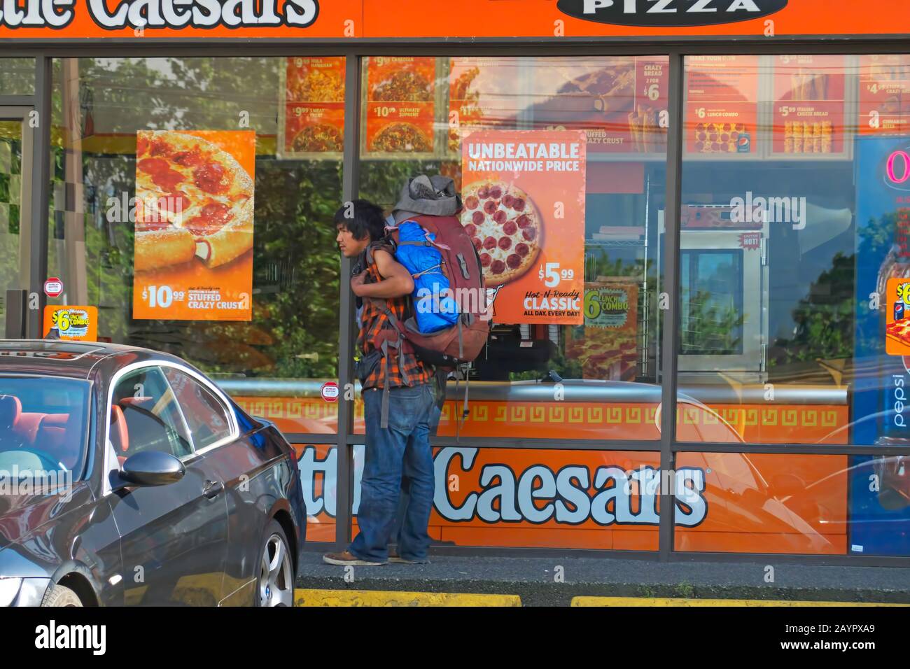 Junger indigener Mann mit Rucksack vor einer Kleinen Caesars Pizza, Vancouver, B. C., Kanada. Stockfoto