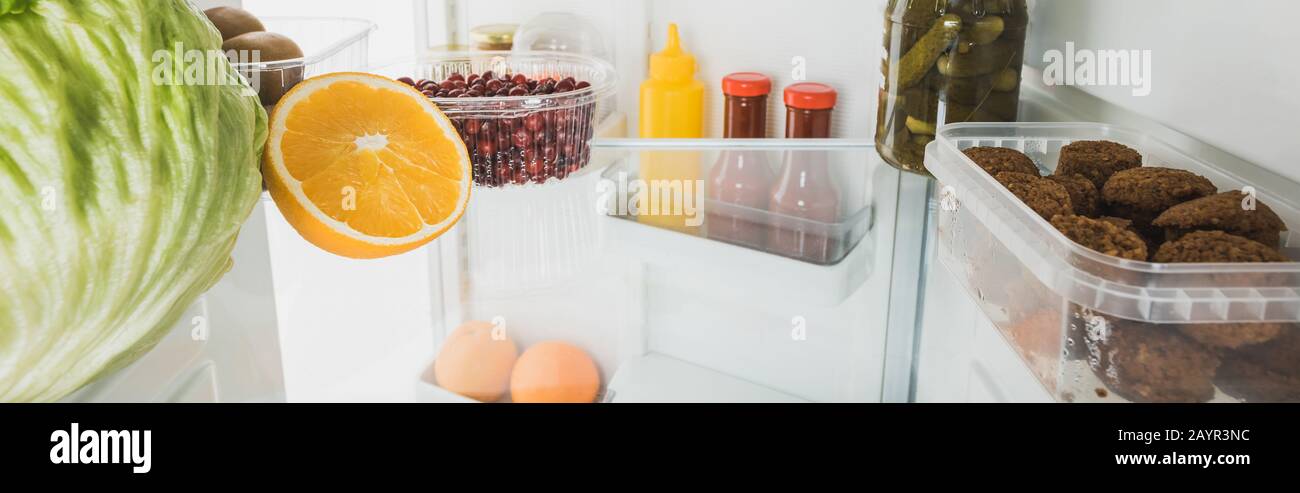 Panoramaaufnahme frischer Früchte mit Kohlschnitzeln und Soßen im Kühlschrank mit offener Tür, isoliert auf weißem Stockbild Stockfoto