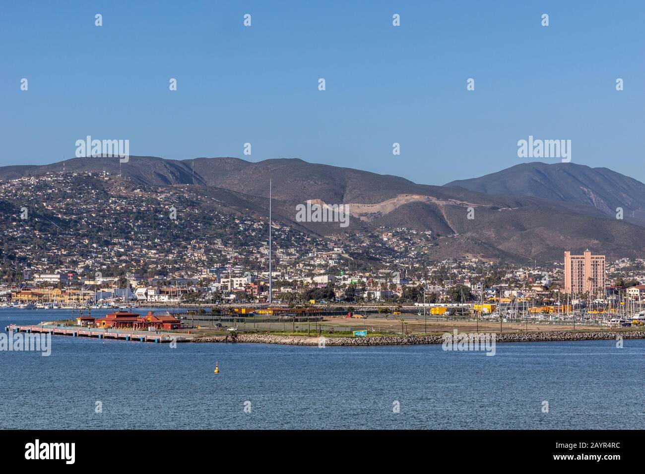 Ensenada, Mexiko - 17. Januar 2012: Red Cruise Terminal am Hafenpier mit Stadtbild am Berghang im Rücken und hinter blauem Erkerwasser. Rosa Stockfoto