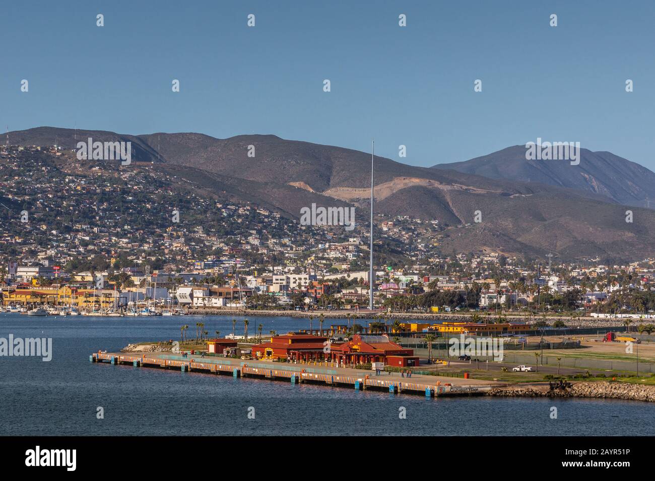 Ensenada, Mexiko - 17. Januar 2012: Red Cruise Terminal am Hafenpier mit Stadtbild am Berghang im Rücken und hinter blauem Erkerwasser. Rosa Stockfoto