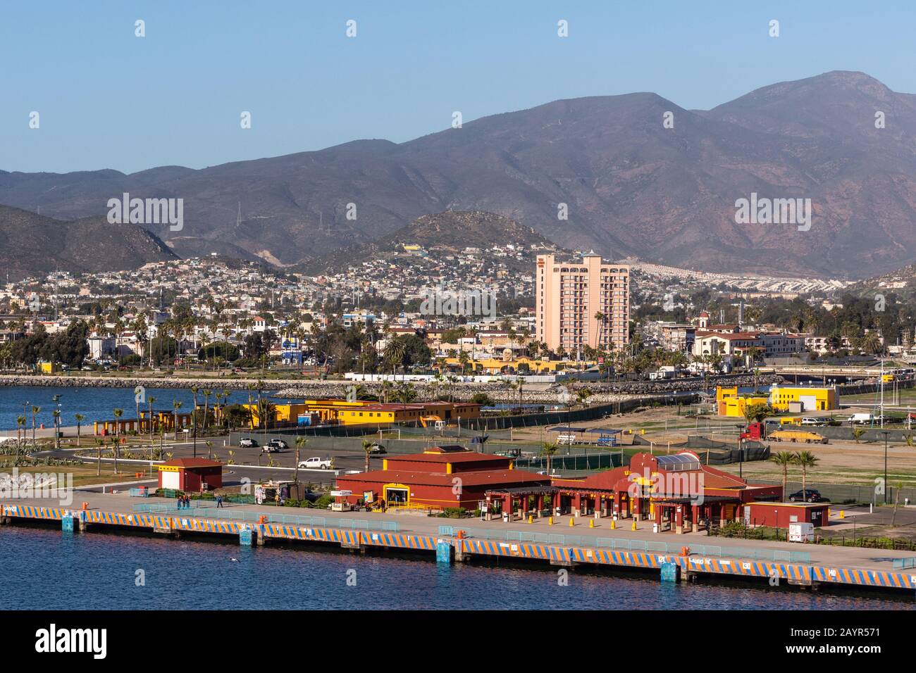 Ensenada, Mexiko - 17. Januar 2012: Nahaufnahme des Red Cruise Terminal am Hafenpier mit Stadtbild am Berghang in der hinteren und hinteren blauen Bucht Stockfoto