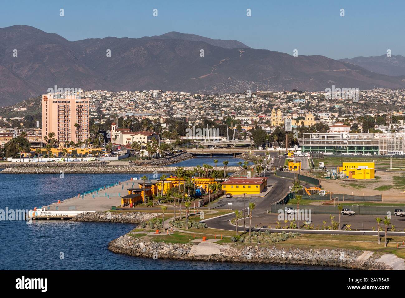 Ensenada, Mexiko - 17. Januar 2012: Hotel in Rosa Tall Villa Marina und gelbe Kathedrale mit ihren Türmen auf der anderen Seite hinter dem Hafen und vor den Städten Stockfoto