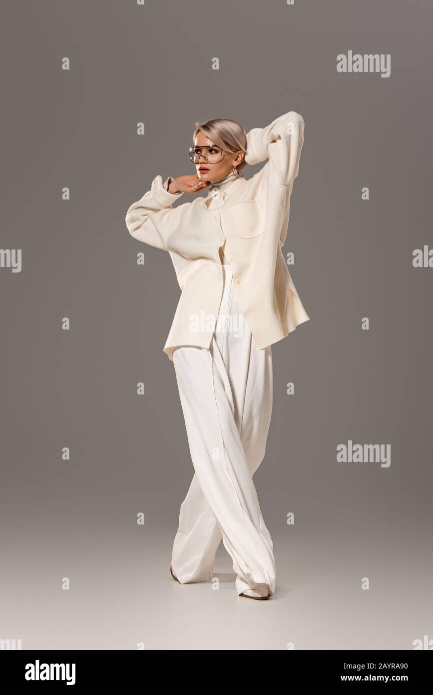 Attraktive Frau in weißem Mantel und Hose mit Blick auf grauen Hintergrund Stockfoto