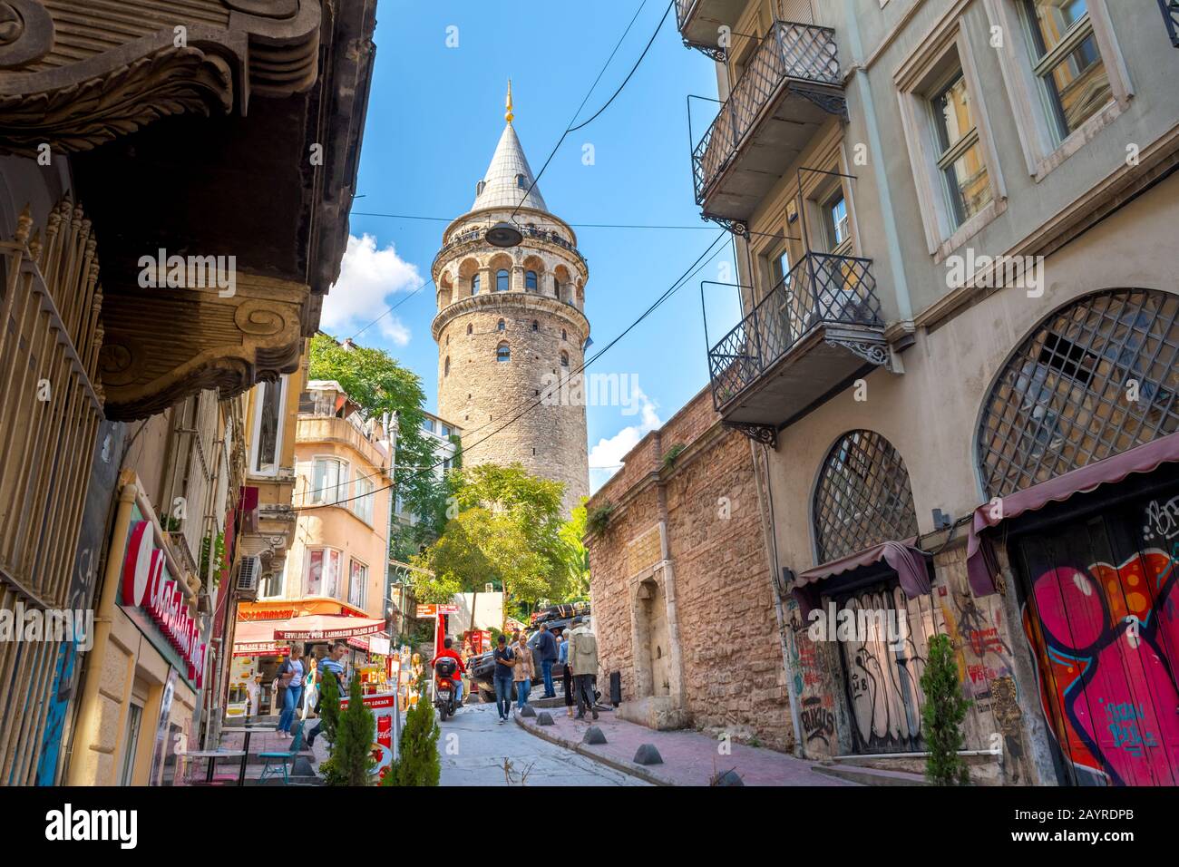Touristen wandern durch die engen, hügeligen Straßen vorbei an Geschäften unter dem historischen Galata-Turm im Karakoy-Viertel in Istanbul, Türkei. Stockfoto