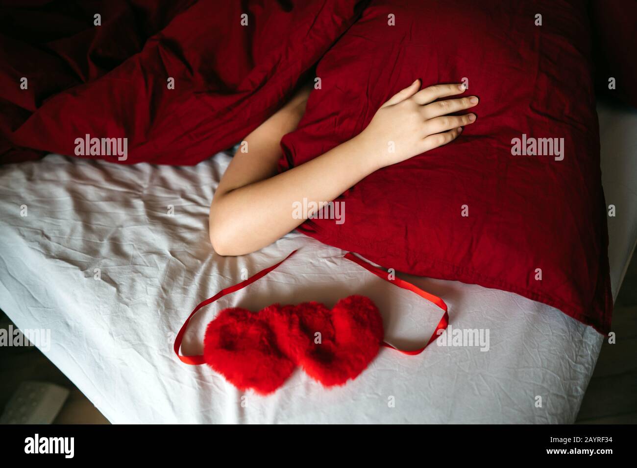 Weibliche Hand, die auf einem roten Kissen liegt, das mit einer Decke bedeckt ist. Stockfoto