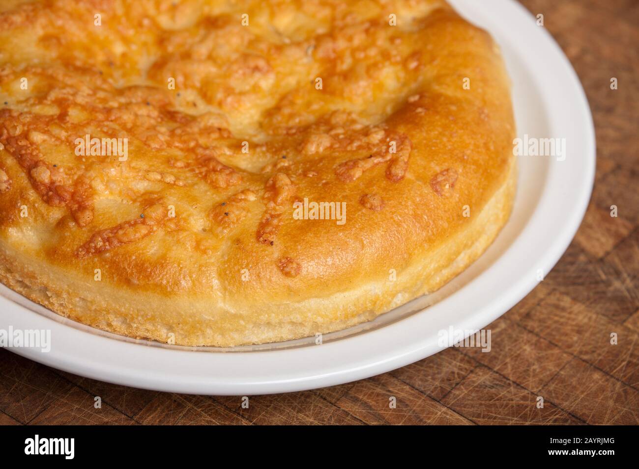 Ganze Laibe mit Focaccia-Brot auf einer weißen Keramikplatte auf einem rustikalen Holztisch Stockfoto