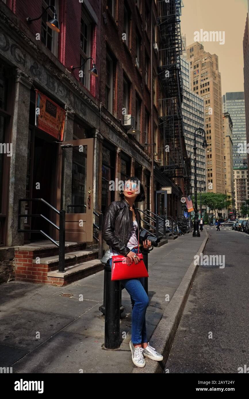 Ein stilvoller Tourist für Asiaten in einer historischen, alten Straße in der Innenstadt Manhattans, die ein Tees mit amerikanischer Flagge und eine blaue Jeans in voller Länge trägt Stockfoto