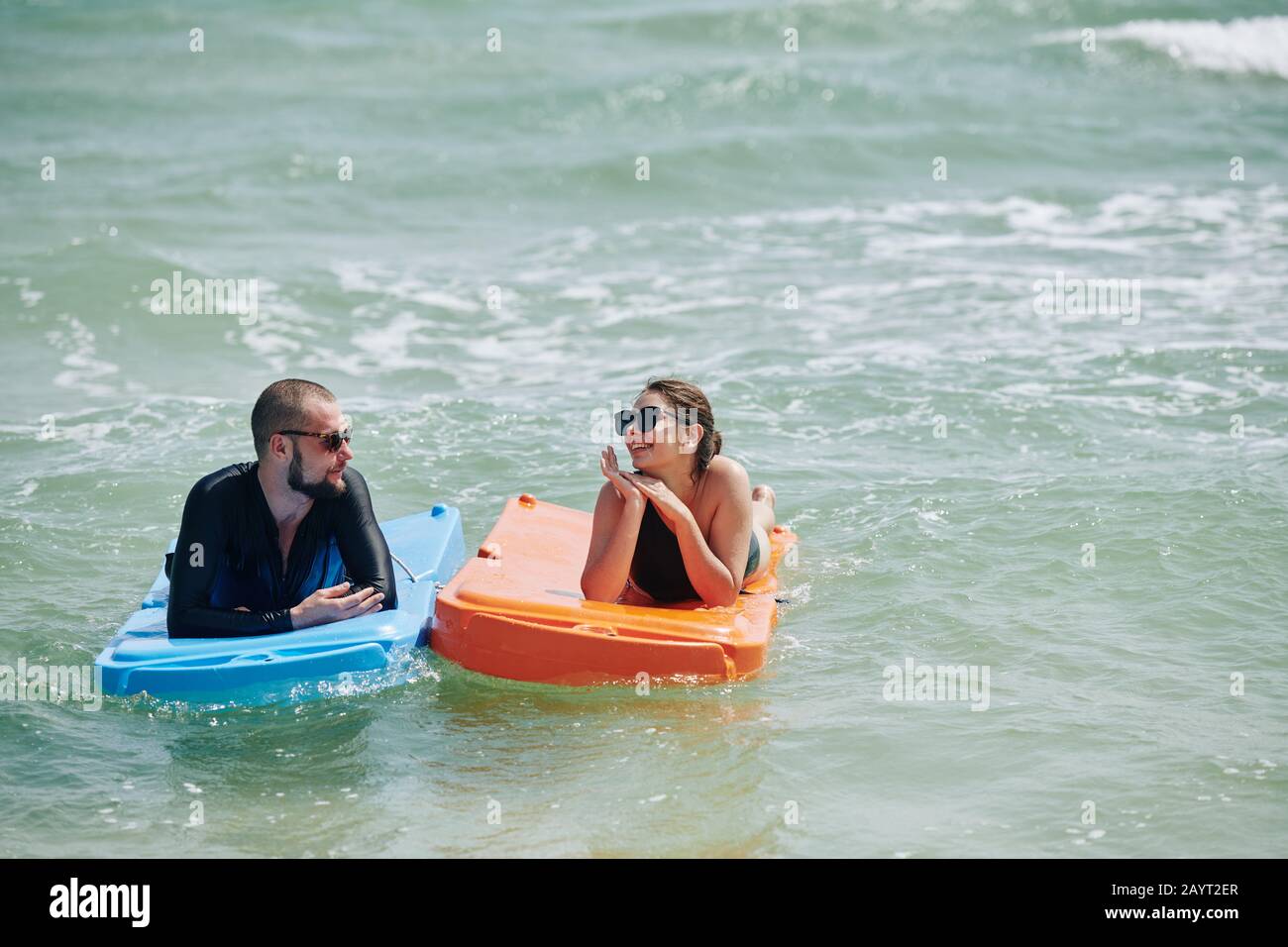 Glücklicher junger Mann und Frau, die sich nach dem Schwimmen im Meerestiergerät in Kunststoffmatratzen ausruhen Stockfoto