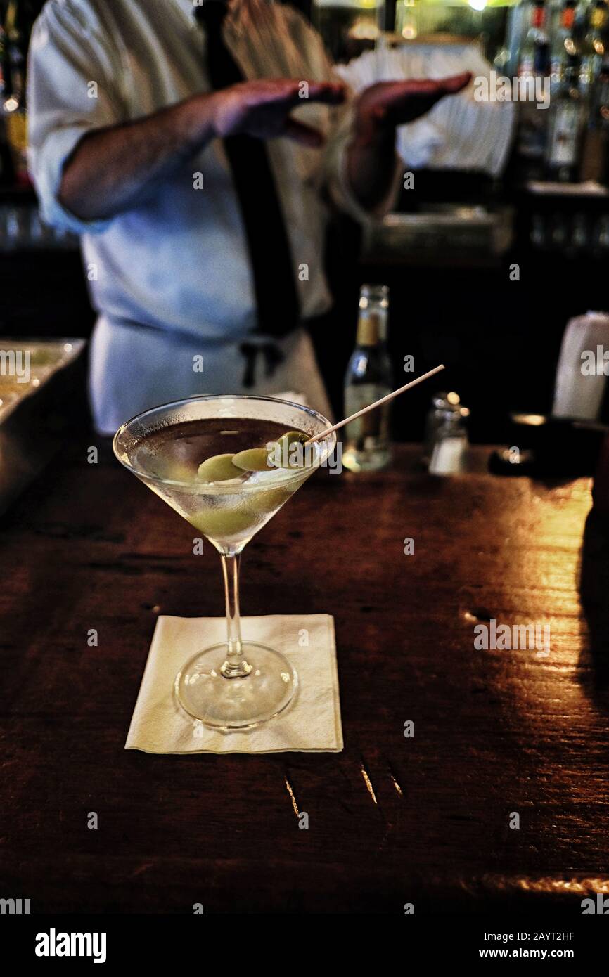 Martini mit drei Oliven an einer alten Holzbar in NYC, die Barkeeper hinter sich Stockfoto