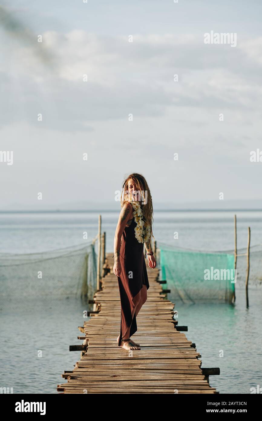 Schöne fröhliche junge Frau mit langen Dreadlocks, die auf einem Holzsteg stehen Stockfoto