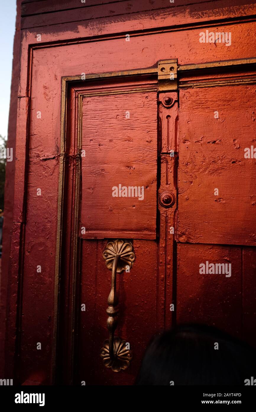 Linke obere Ecke einer ungewöhnlichen alten Holztür mit Messinggriff, Holzplatten und Einlegezierleiste, die in Metallic-Rot lackiert ist, in Greenwich Village NYC Stockfoto