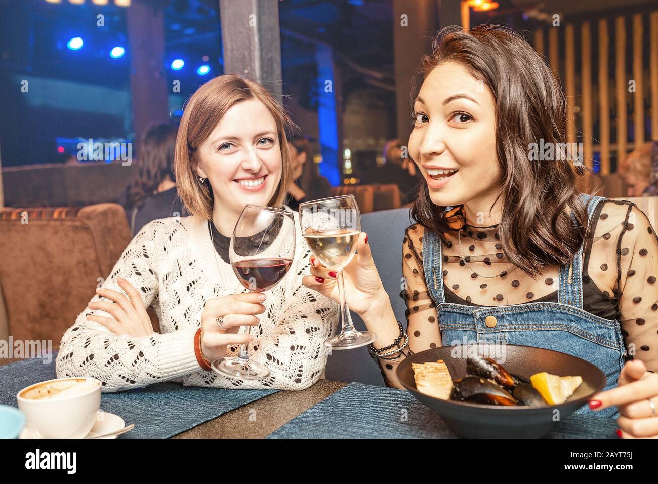 Zwei Freundinnen haben Spaß und unterhalten sich, während sie ein Glas Wein in einem Restaurant in einem Nachtclub trinken. Das Konzept der Entspannung und der Frigschaft Stockfoto