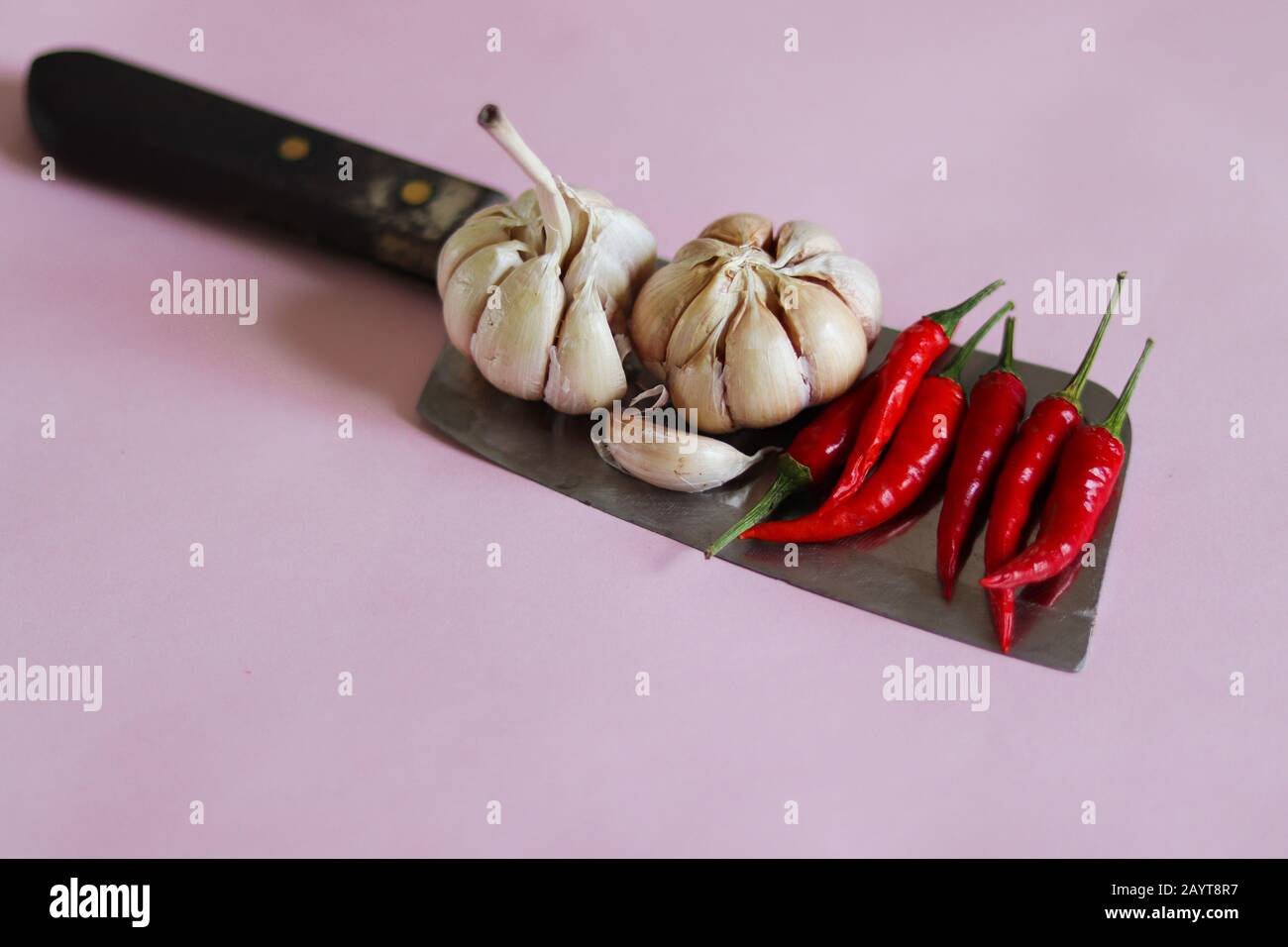 Knoblauchzwiebeln und rote Chilischoten auf einem Messer vor einem rosafarbenen Hintergrund, um das Konzept der Gastronomie, Küche, Küche und Lebensmittelindustrie zu zeigen Stockfoto