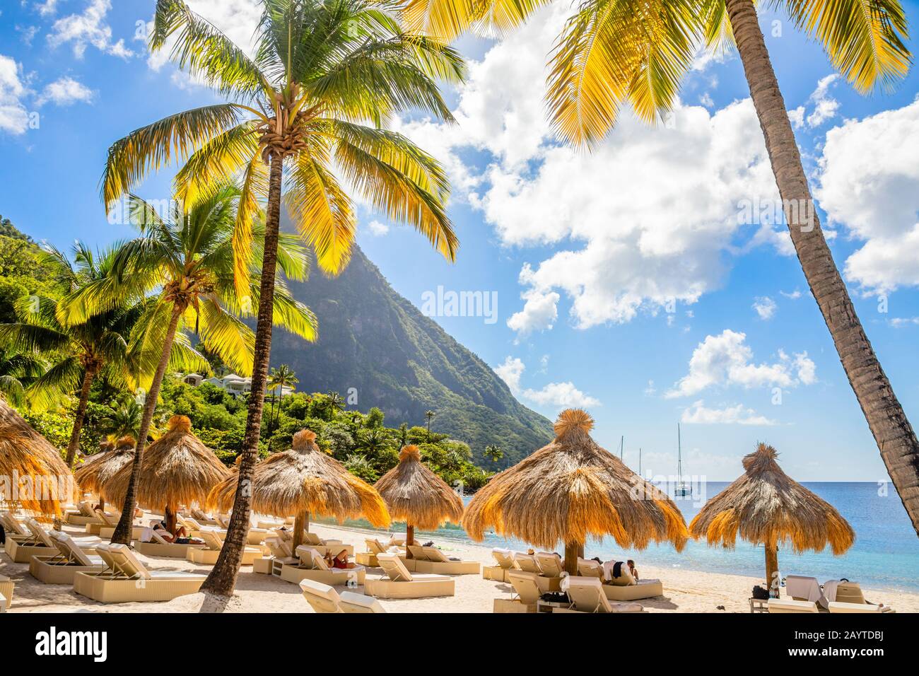 Karibischer Strand mit Palmen und Strohumrellas am Ufer mit Berg Gros Piton im Hintergrund, Zuckerstrand, St. Lucia Stockfoto