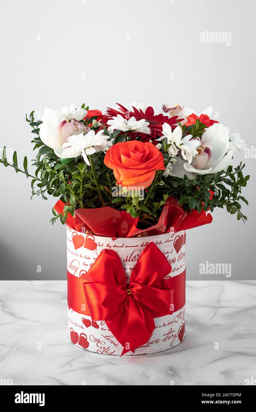 Blumenstrauß mit bunten Blumen in einer Schachtel mit rotem Bandbogen auf grauem Hintergrund. Geschenk, Grußkarte Stockfoto