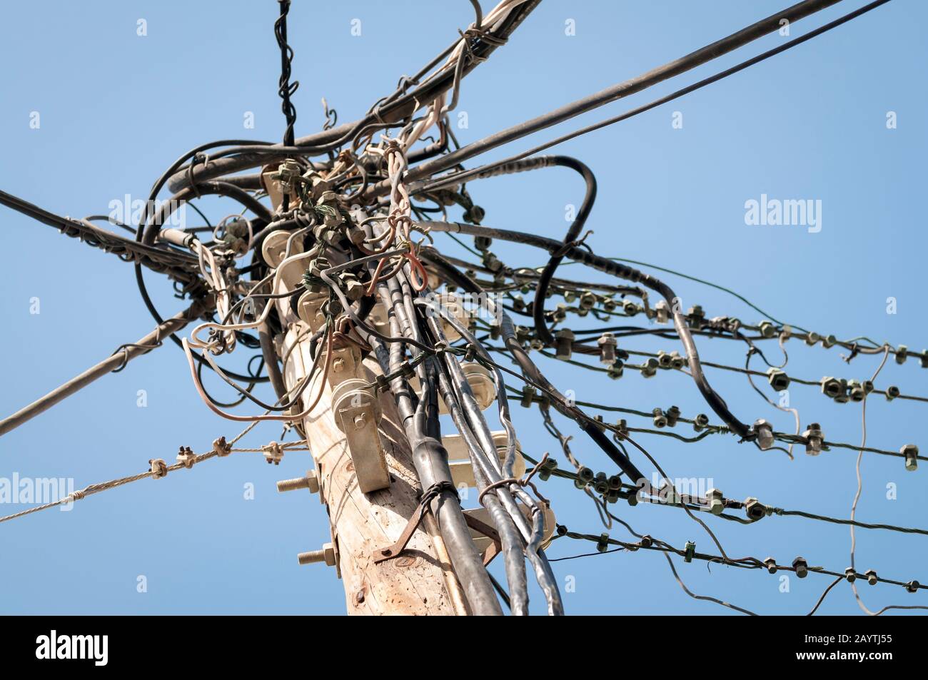 Elektro- und Telefonkabel und in massivem Gewirr auf einem Holzpfosten gegen den blauen Himmel Stockfoto