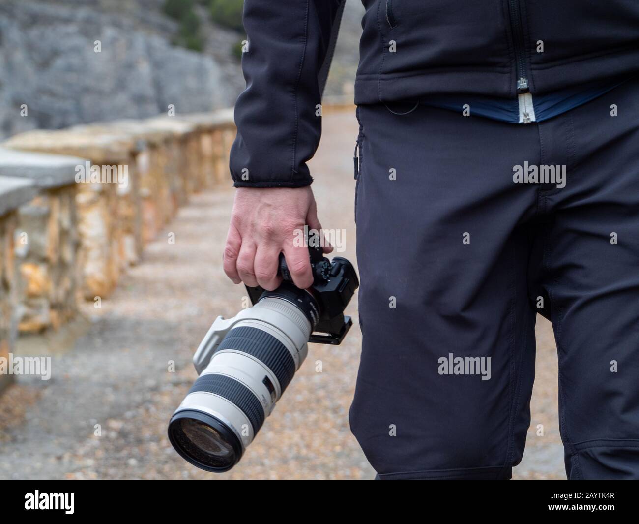 Hand eines Mannes, der eine Kamera mit einem großen Zoomobjektiv im Freien inmitten eines Pfades hält, der von kleinen Steinsäulen in Maderuelo in Spanien umgeben ist Stockfoto