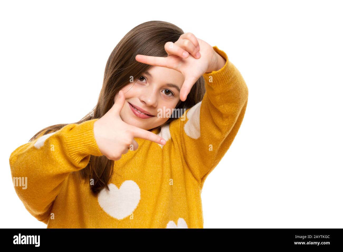 Entzückendes Mädchen im Elementaralter, das lächelt, während er die Kamera betrachtet und die Handgeste des Bilderrahmens macht. Studio auf weißem Hintergrund aufgenommen. Stockfoto