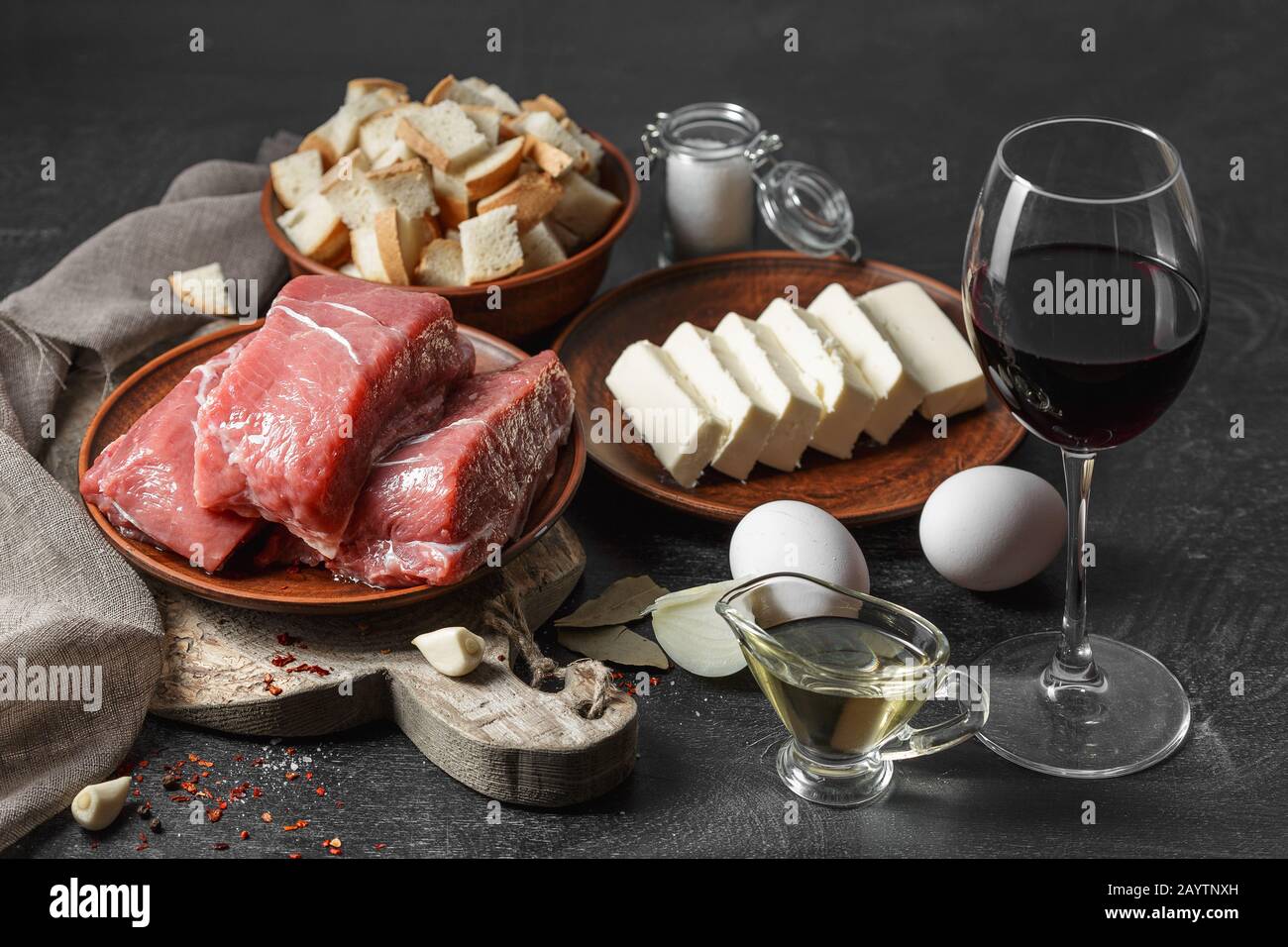 Lebensmittelzutaten, frisches rohes Rindfleisch, Butter, Eier, Öl, Brot, Rotwein auf schwarzem Holztisch Stockfoto