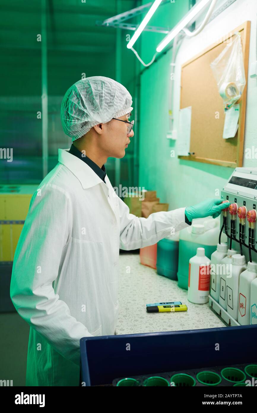 Seitenansicht Porträt asiatischer Arbeiter, die Schutzkleidung tragen, die im Biolabor arbeitet, das durch grünes Licht beleuchtet wird Stockfoto