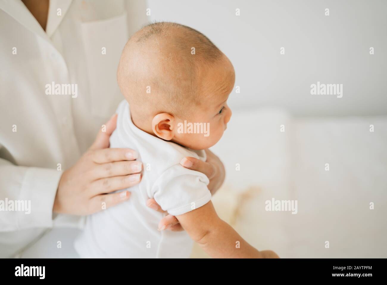 Von oben, als die Mutter den liebenswerten neugeborenen Sohn pattert, der das asiatische Baby zu Hause auf dem Bett massiert Stockfoto