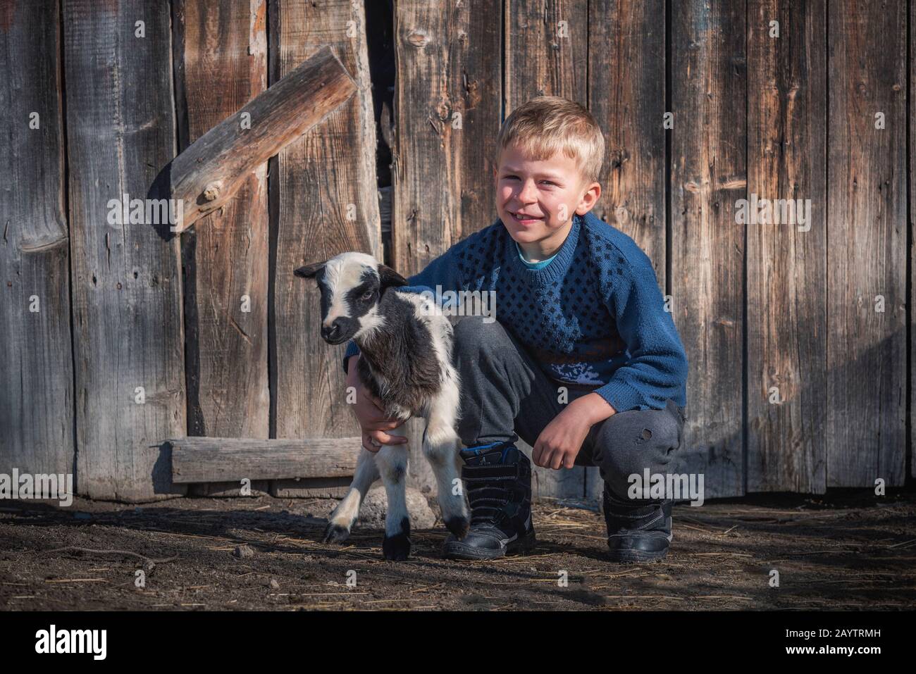 Krastava Dorf, Rhodope Berge / Bulgarien: Porträt des kleinen Jungen Umarmung Lamm auf dem Hof. Stockfoto