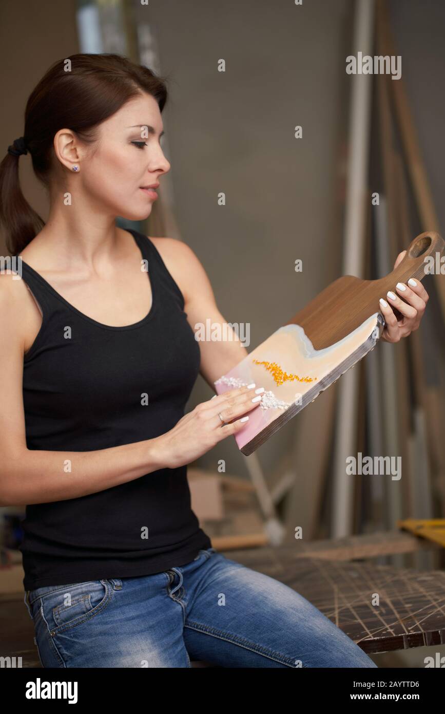 Brünette Frau mit Bild auf Schneidebrett sitzt in der Werkstatt auf dem Tisch Stockfoto