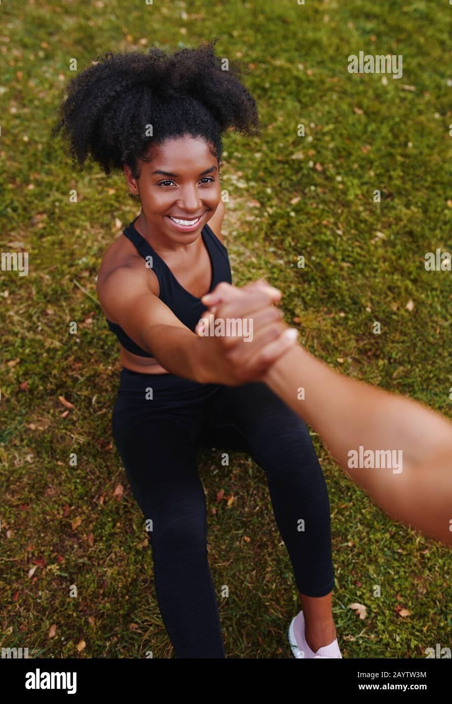 Eine obige Ansicht der lächelnden afroamerikanischen, sportlichen jungen Frau, die während des Trainings im Park Hilfe von ihren Freunden erhält Stockfoto